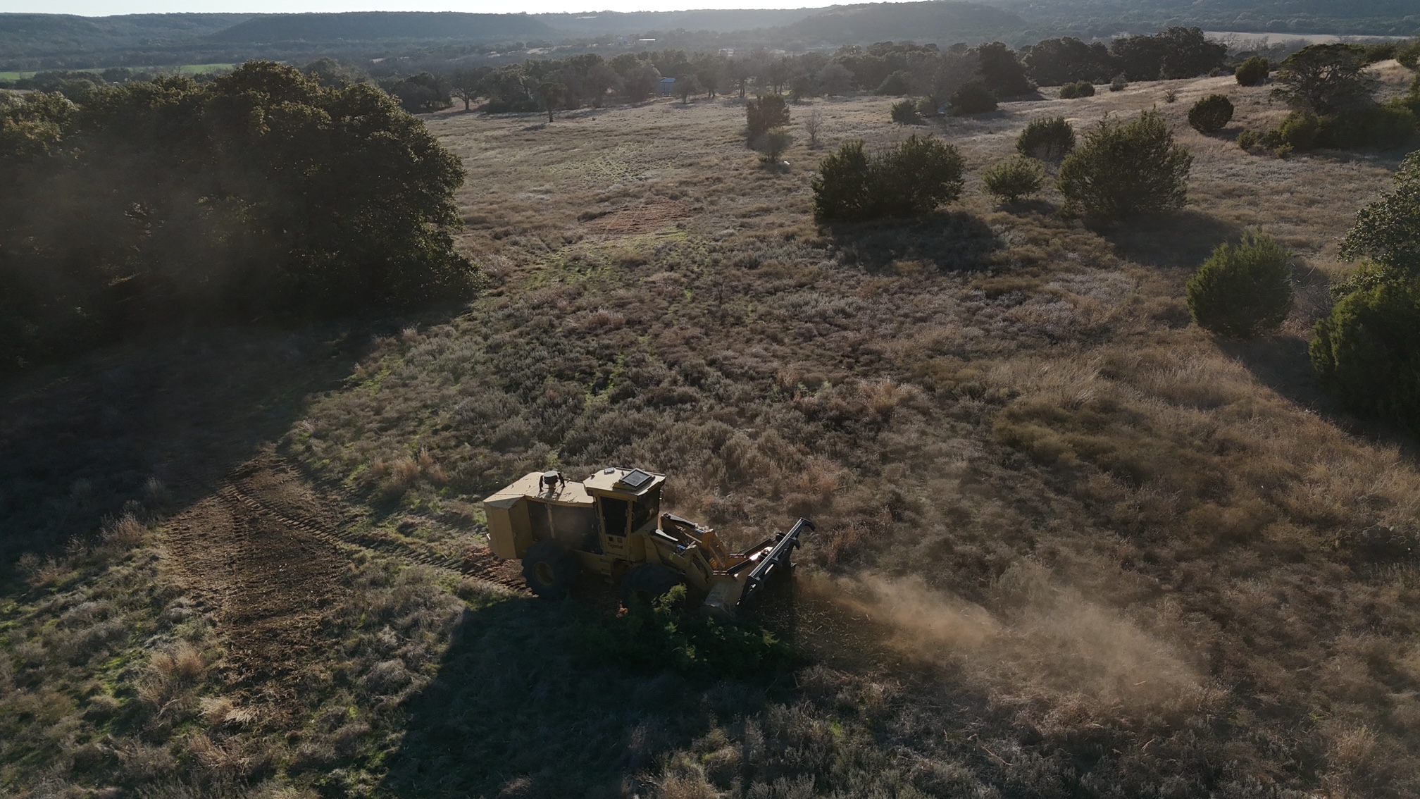 Cedar Eater mulching machine grinding a Cedar  tree into mulch.  Revealing an open pasture with the sunset.